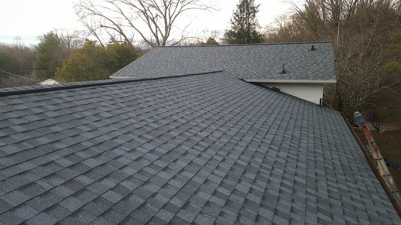 Gray asphalt shingle roof on a residential house with trees in the background.